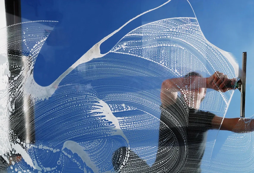 window with cleaning agent on it being squeegeed with a blue sky behind.